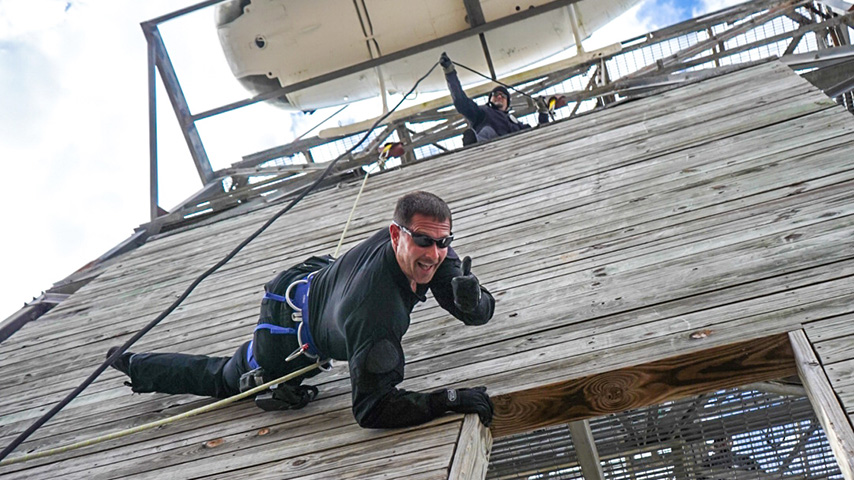 An officer gives a thumbs up while rapelling down a practice tower
